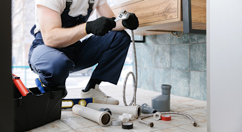 A plumber sitting on the ground to repair a shower hose in the bathroom.