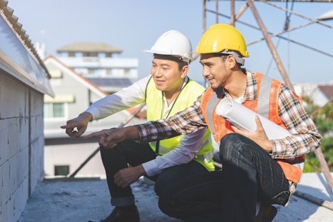 This image shows a builder and a general contractor wearing high visibility vests and hard hats looking at something together on a construction site.