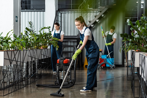 This image shows professional cleaners using a vacuum cleaner and mop to clean a modern office building.