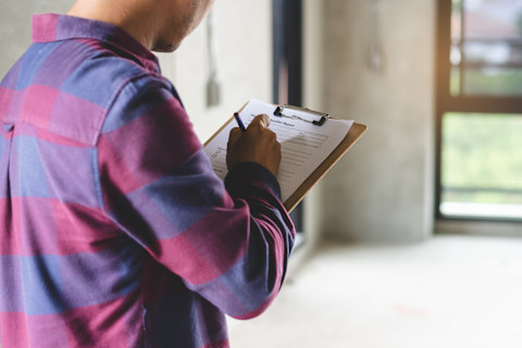 This image shows a home inspector carrying out an inspection in an unfurnished home. He is noting down information on a clipboard.