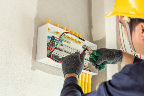 An electrician installs new electrical outlets in a modern interior. Tools and wiring are visible during the installation.