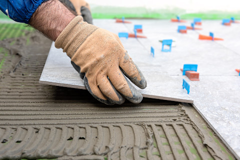 A bricklayer places tiles on a new floor surface. The tiles are aligned carefully with adhesive.