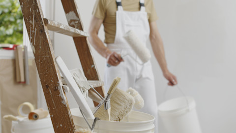 Paint and tools are visible, and a ladder and a painter preparing to paint a room