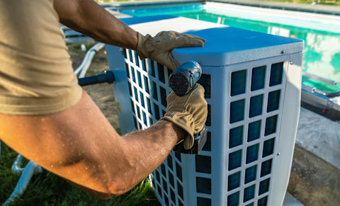 This image shows a HVAC technician installing a pool heater in a backyard.