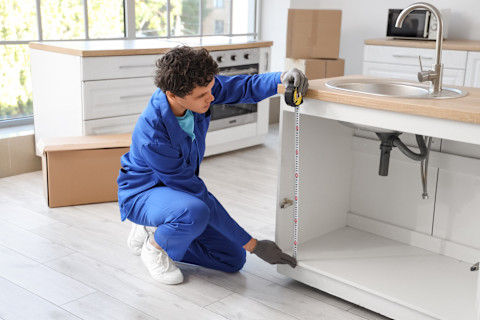 A professional is measuring some cabinets to size