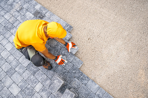 A construction worker places gray paving stones carefully. The stones form a neat outdoor surface.