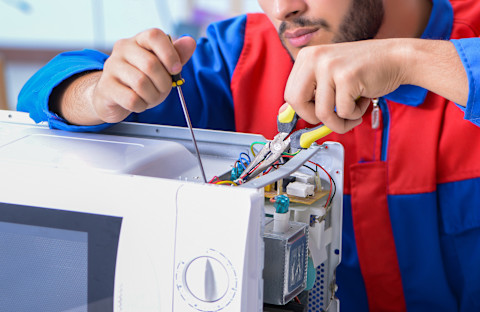 A young repairman fixes a microwave oven indoors. The appliance is open to access internal components.