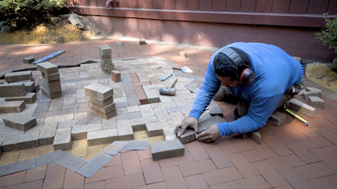A brick paver sets bricks into place on the ground. The pattern is carefully adjusted.