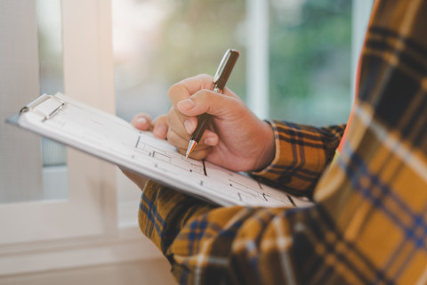 This image is a close up of a tradesperson holding a clipboard and pen while conducting a home inspection.
