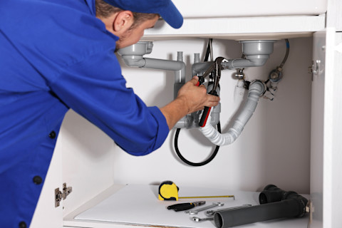 A professional plumber repairs a home piping system. Pipes and fittings are exposed during the fix.