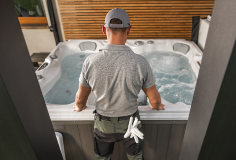 Technician performing hot tub installation and inspection on an outdoor deck. Professional hot tub setup, maintenance, and service for home spas. Quality hot tub installation ensuring safe and optimal performance.