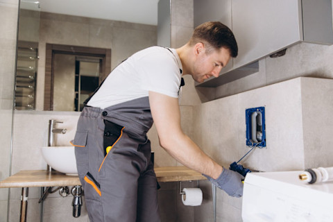 A professional plumber repairs a concealed toilet system inside a bathroom wall.