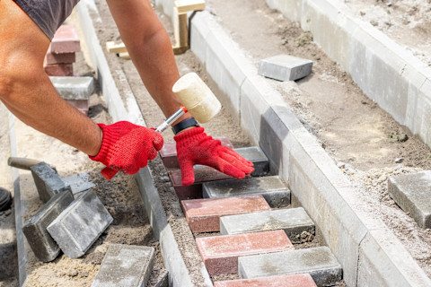 Paving contractor lays stones on a new pathway. The ground is prepared for even placement.