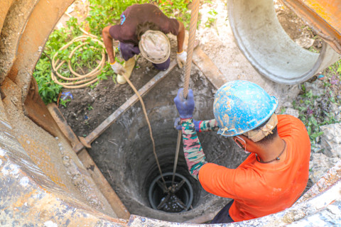 This image shows two construction workers wearing hardhats feeding steel rope into a water well.